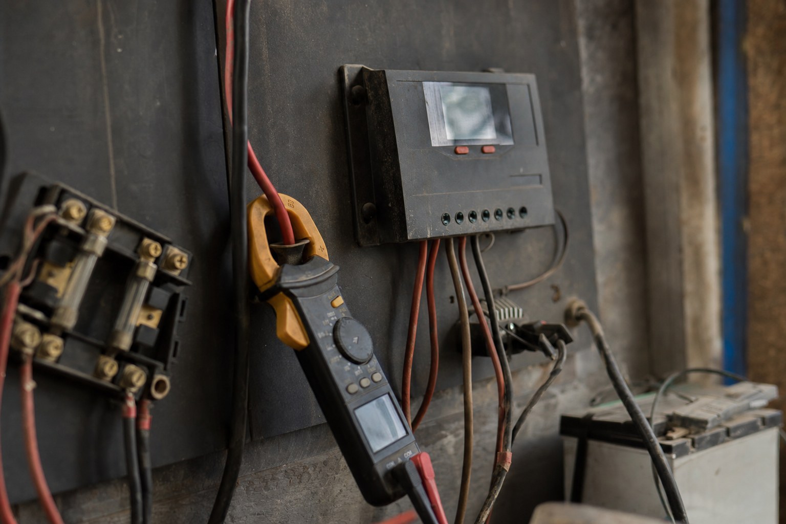 A digital clamp meter reading a wire beside a solar charge controller display and neat cabling.
